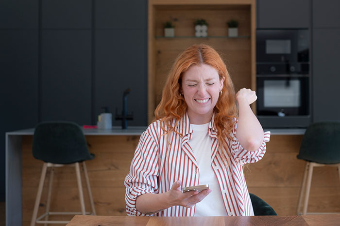 Woman with red hair showing frustration holding phone in modern kitchen