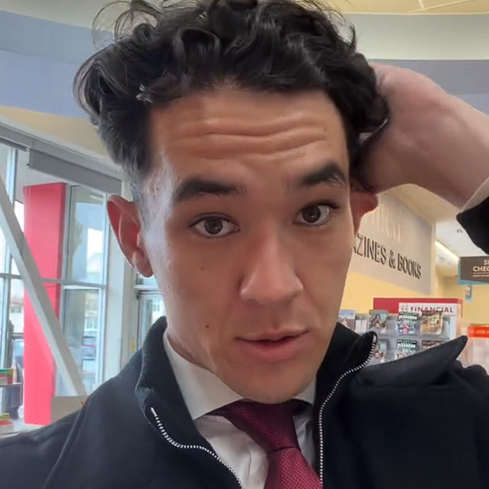 Young man indoors adjusting hair with books in background