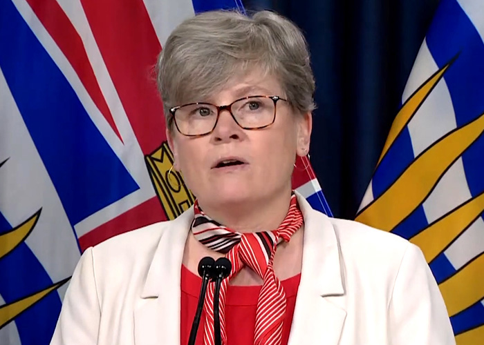 Woman speaking at press conference with British Columbia flags