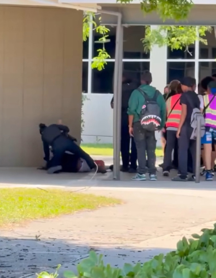 Group of students watching female cop restrain high school boy outside school Group of students watching female cop restrain high school boy outside school