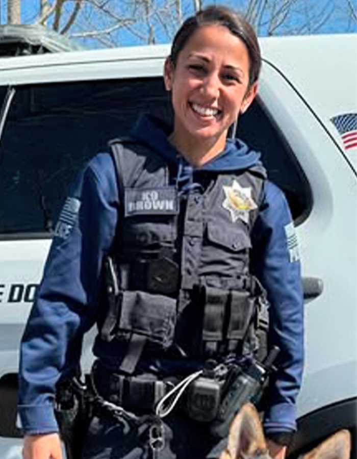 Female police officer in tactical vest smiling outside with police dog Female police officer in tactical vest smiling outside with police dog