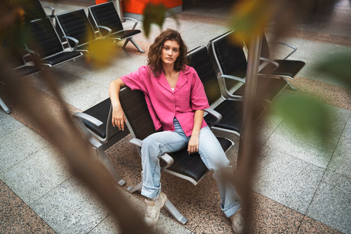 Woman in pink shirt sitting in airport chairs, reflecting on cyberbullying and body-shaming