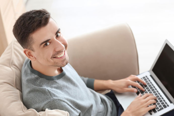 Smiling man using laptop engaging in cyberbullying activity online