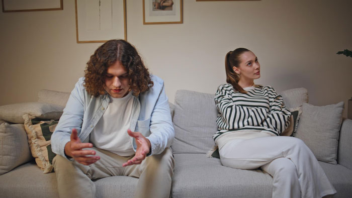 Couple sitting apart on couch looking upset after cyberbullying argument