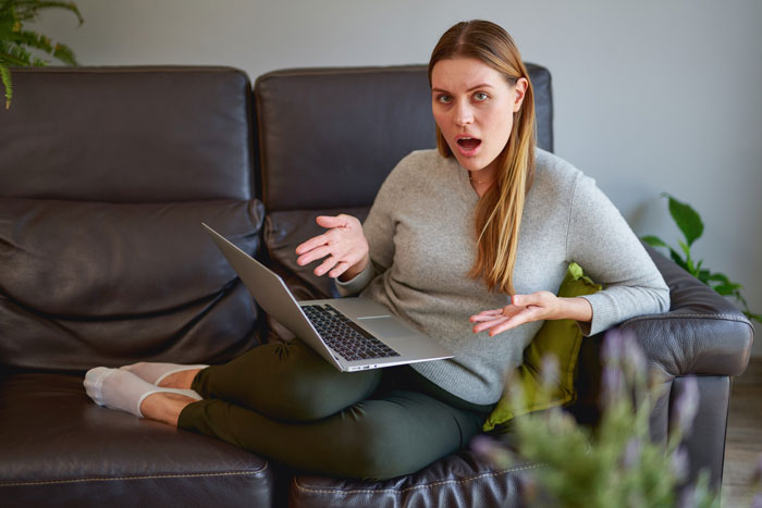 Shocked woman on couch reacting to cyberbullying content on laptop