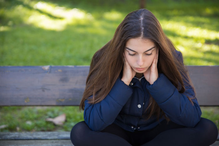 Sad woman sitting on bench reflecting on financial struggles Sad woman sitting on bench reflecting on financial struggles