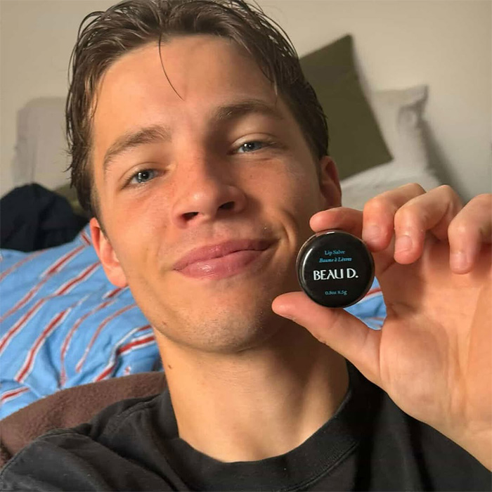 Man holding Beau D. lip salve container smiling at camera