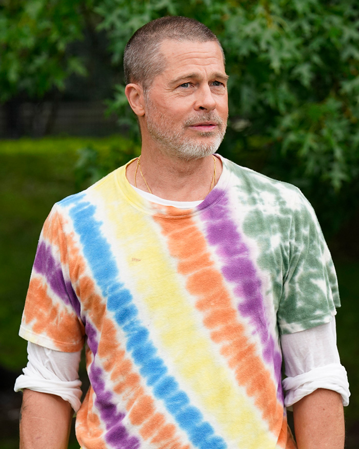 Brad Pitt wearing tie-dye shirt outdoors with greenery in background