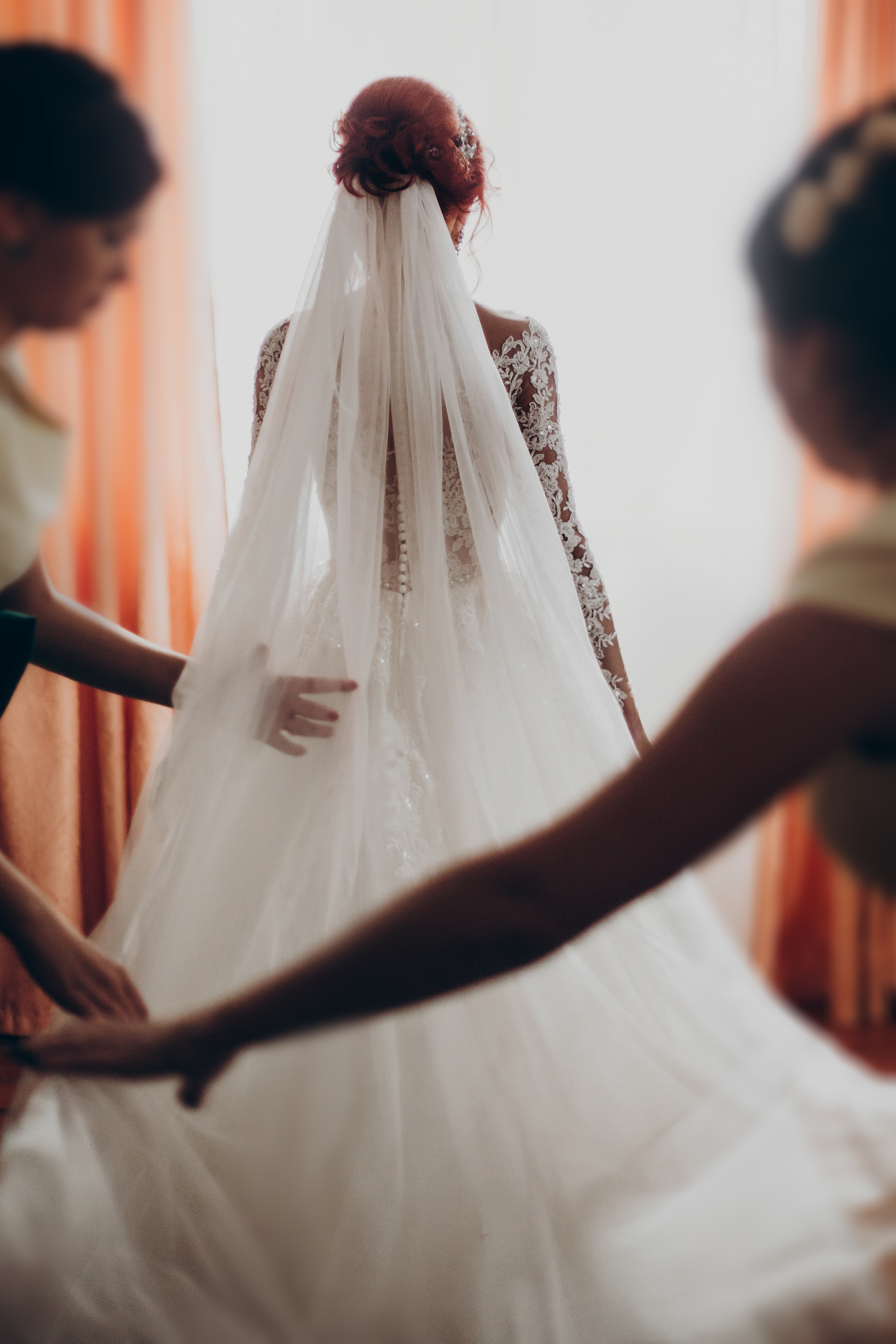 Bride wearing lace wedding gown with long veil assisted by bridesmaids before ceremony Bride wearing lace wedding gown with long veil assisted by bridesmaids before ceremony