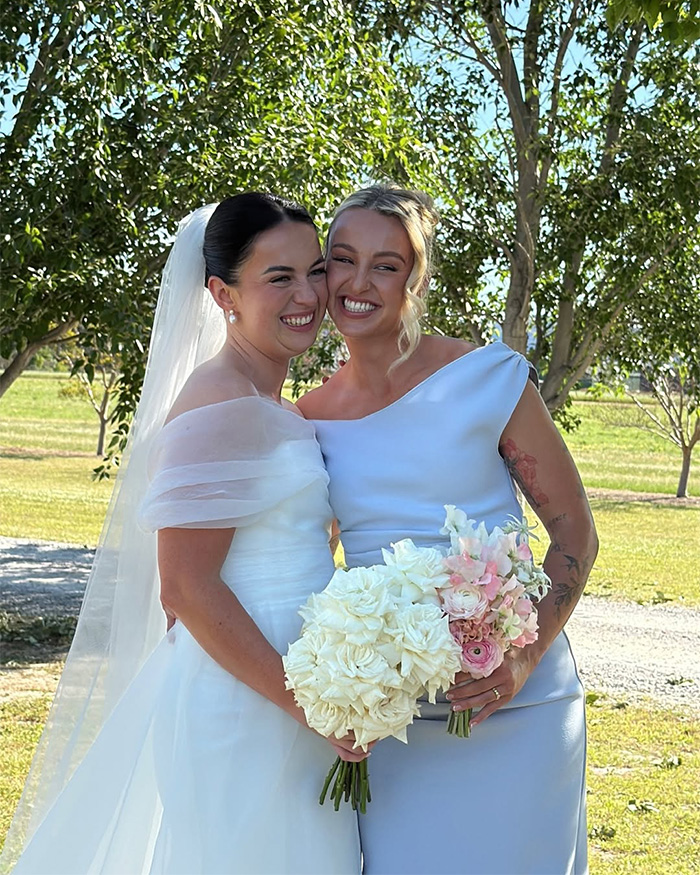 Bride and bridesmaid smiling outdoors holding wedding bouquets