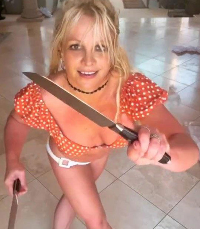 Britney Spears holding a large knife indoors wearing an orange polka dot top