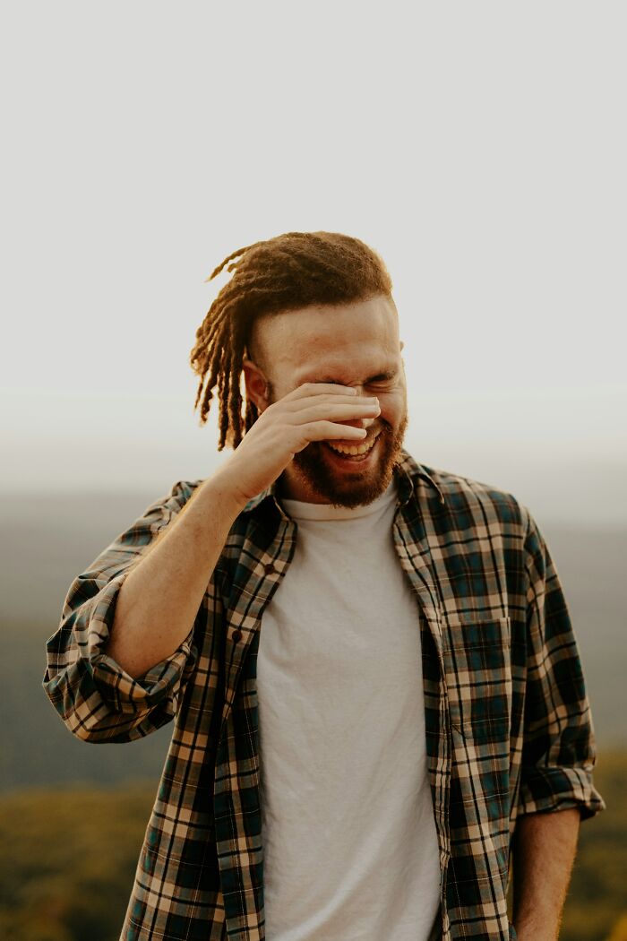 Man laughing covering his face with hand during outdoor sunset