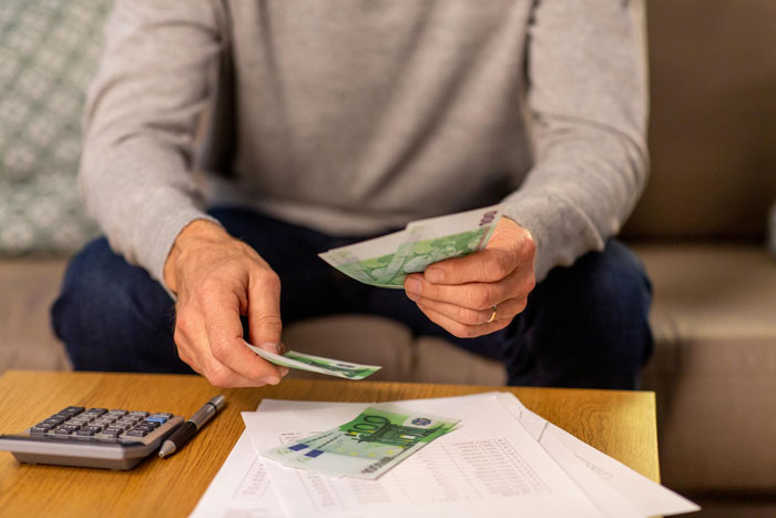 A person's hands counting money with a calculator and papers on a table, representing wedding money and food expenses.