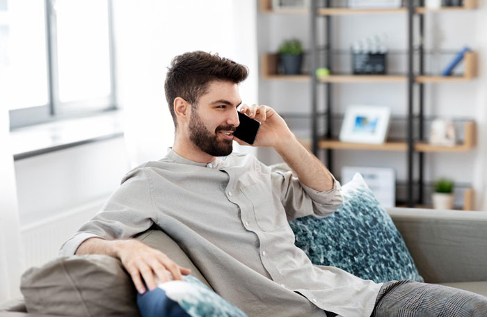 Man on a couch talking on the phone about brother wedding money, food arrangements.