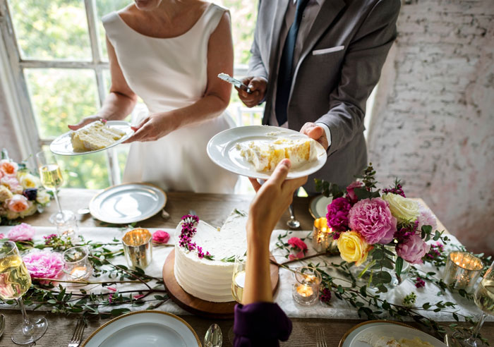 A bride and groom serve wedding cake to guests at a decorated table, highlighting the wedding catering aspect.