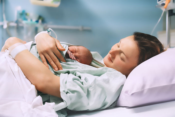 Mother holding newborn baby in hospital bed during postpartum recovery Mother holding newborn baby in hospital bed during postpartum recovery