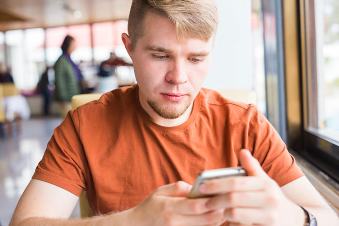Young man in orange shirt using phone focusing on screen