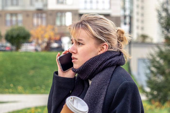 Woman with cup and scarf making phone call outdoors about bullying situation