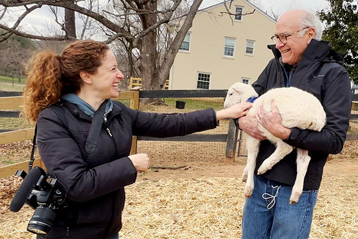 Vermont farmer holding goat while woman smiles outdoors on farm