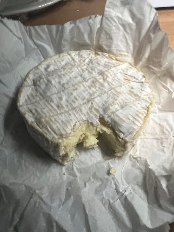 Round wheel of camembert cheese with a bite taken out on paper