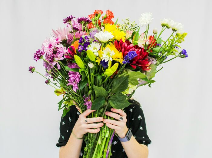 Person holding large colorful bouquet of flowers hiding face