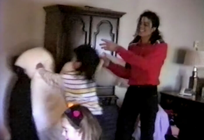 Michael Jackson smiles in a red shirt while children play with pillows; 60 Minutes accusations.