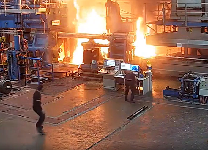 Machinery failure: A factory floor engulfed in large flames as two workers observe the catastrophic event from a control station.