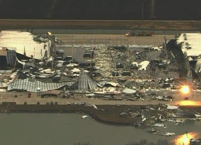 Aerial view of a structure that has failed catastrophically, showing widespread destruction near a body of water.