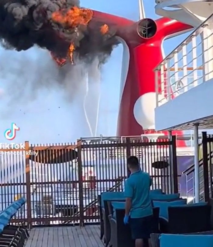 A red cruise ship's funnel is on fire, emitting thick black smoke. This machinery failure is catastrophic.