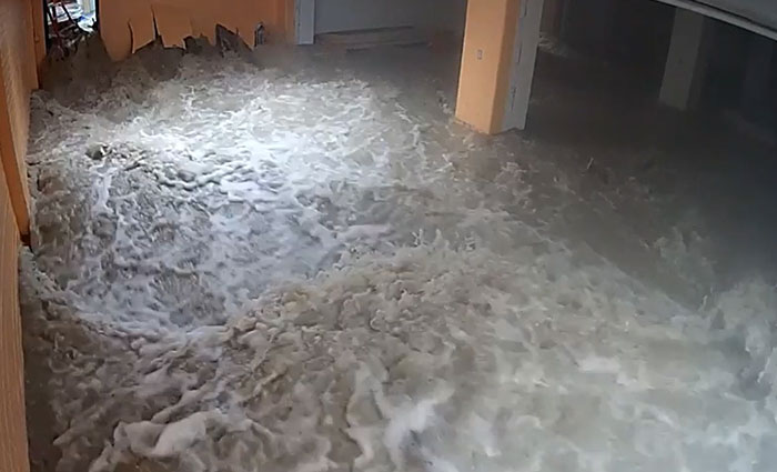 Floodwaters rushing into an indoor space, creating white foamy waves, a catastrophic failure of structures.