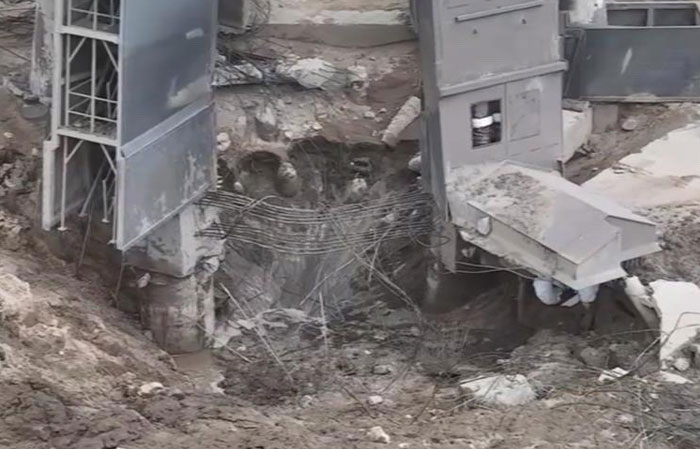 Two large grey machinery structures collapsing into a deep, muddy pit, showing catastrophic failure of the support system.