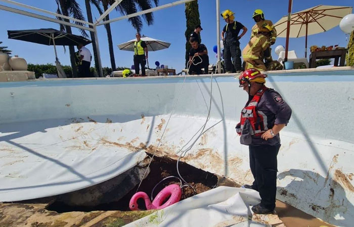 Rescuers at a swimming pool with a catastrophic failure, a sinkhole opening up, revealing a pink flamingo float.