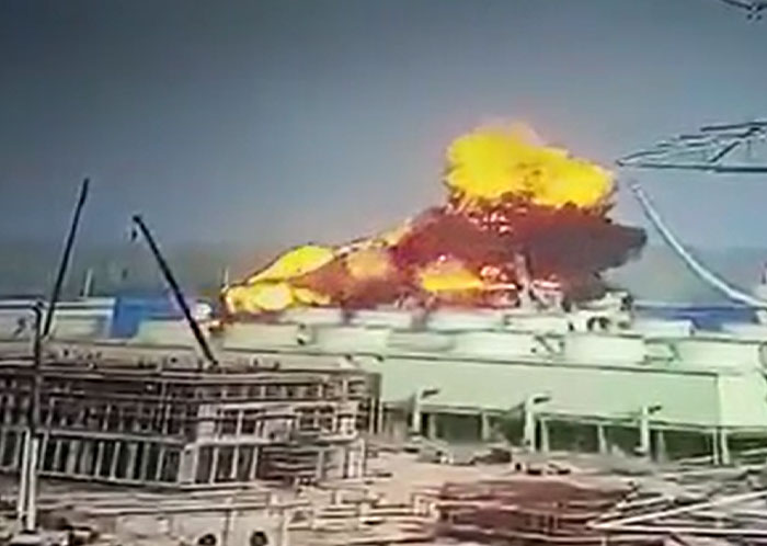 A large, catastrophic failure, fiery explosion engulfing a structure at a construction site against a clear sky.