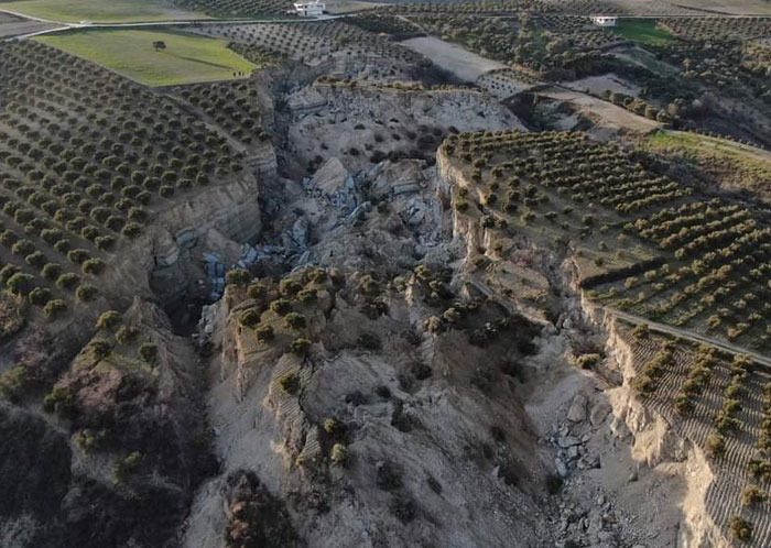 Aerial view of a catastrophic landscape failure, with massive cracks and collapsed earth cutting through agricultural fields.