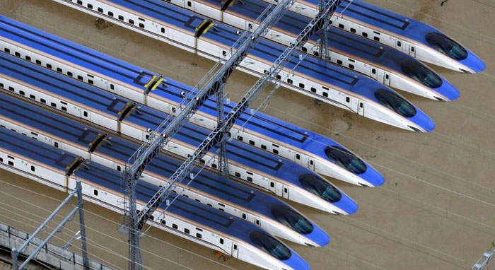 Overhead view of multiple blue and white bullet trains partially submerged in floodwaters, a machinery failure.