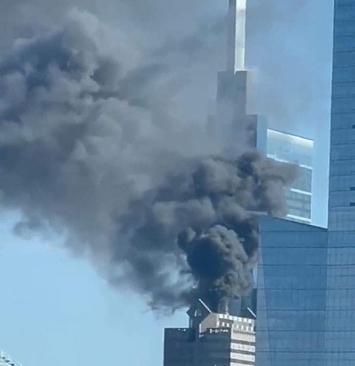 Thick black smoke billowing from a tall skyscraper, a structure that has failed catastrophically.