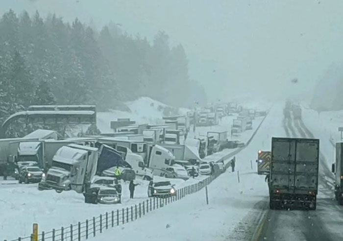 A catastrophic machinery failure with multiple semi-trucks piled up on a snow-covered highway during a blizzard.