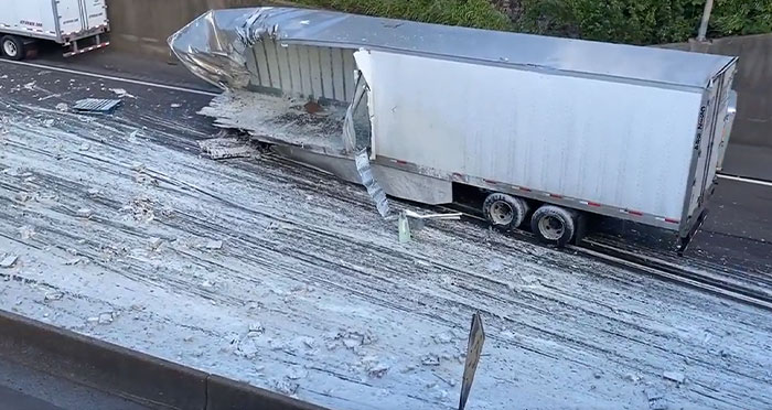 A trailer truck after machinery failure, collapsed on its side on a road with white debris strewn everywhere.