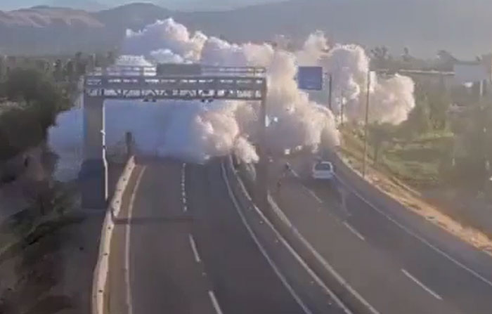 Large white smoke plume over a highway, indicating machinery or structures have failed catastrophically.