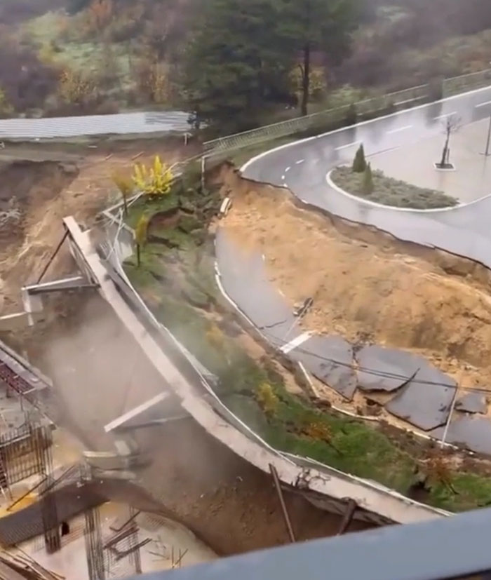 Aerial view of a road and adjacent land that have failed catastrophically due to a landslide, with cracked asphalt.