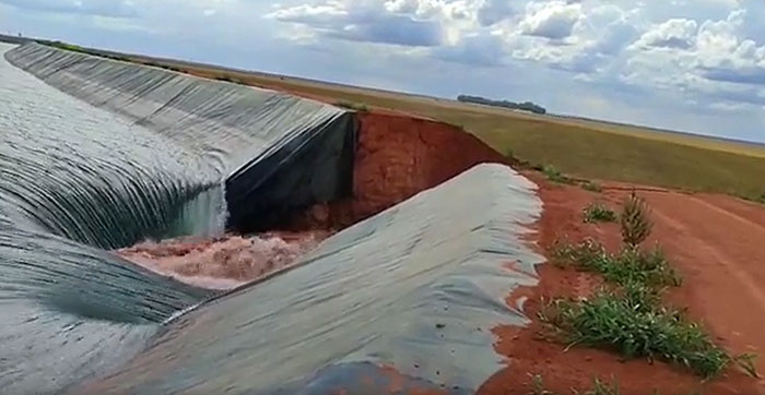 Water gushing from a ruptured black liner, creating a muddy torrent, a catastrophic failure of structures.