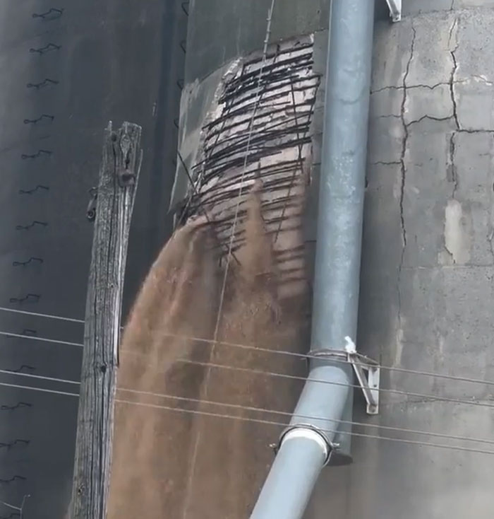 Grain silo machinery catastrophically failed, spilling contents. Exposed rebar and cracked concrete show structural damage.