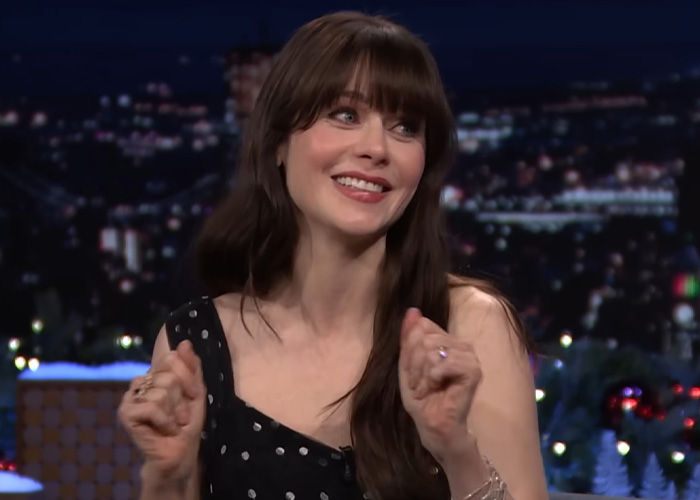 Zooey Deschanel smiling on a talk show, illustrating celebrity saving habits and ways to be frugal.