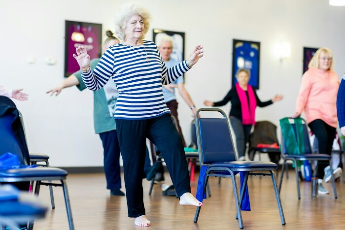 A group of science professionals and others exercising, an older woman in a striped shirt balancing on one leg, showing cool facts about fitness.