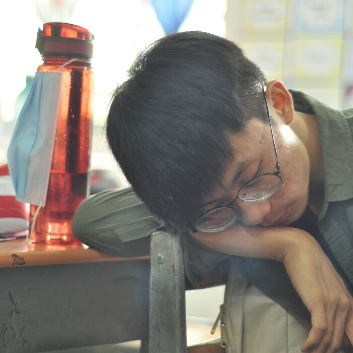 A student in glasses asleep on a desk, next to a water bottle with a face mask. Relatable content for epic comebacks.