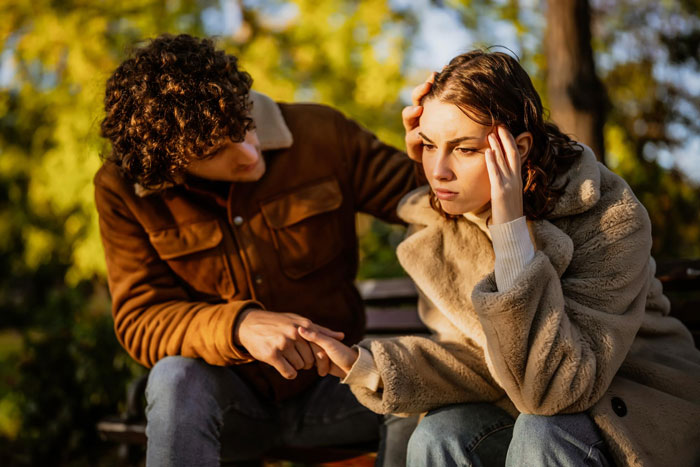 A distraught woman, clutching her head, as a man tries to comfort her. Could this be about a cheating partner?