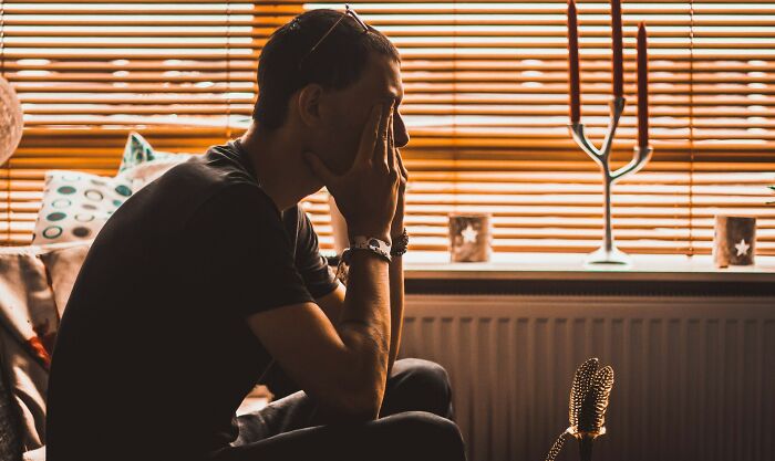 A man in a dark shirt, head in hands, looking stressed, with a vintage microphone nearby. Men suffering and manosphere content.