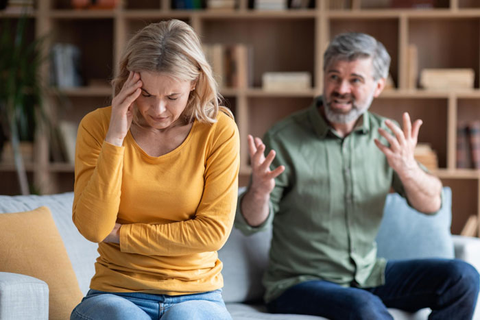 A distressed woman holds her head while a man behind her gestures angrily. The woman is expected to be a maid.