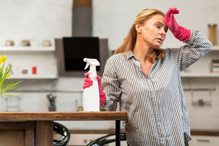 A stressed woman wearing pink cleaning gloves holds a spray bottle, looking exhausted as a maid.