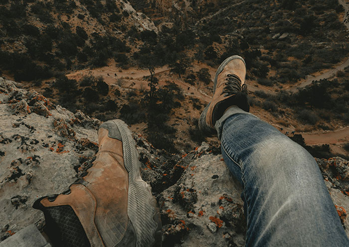 Person sitting on edge of cliff with hiking boots showing close encounter with passing away